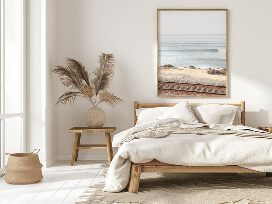 A framed print of a beach scene with waves and surfers, displayed on a train track in Del Mar, San Diego. Photograph in minimalist mock up.