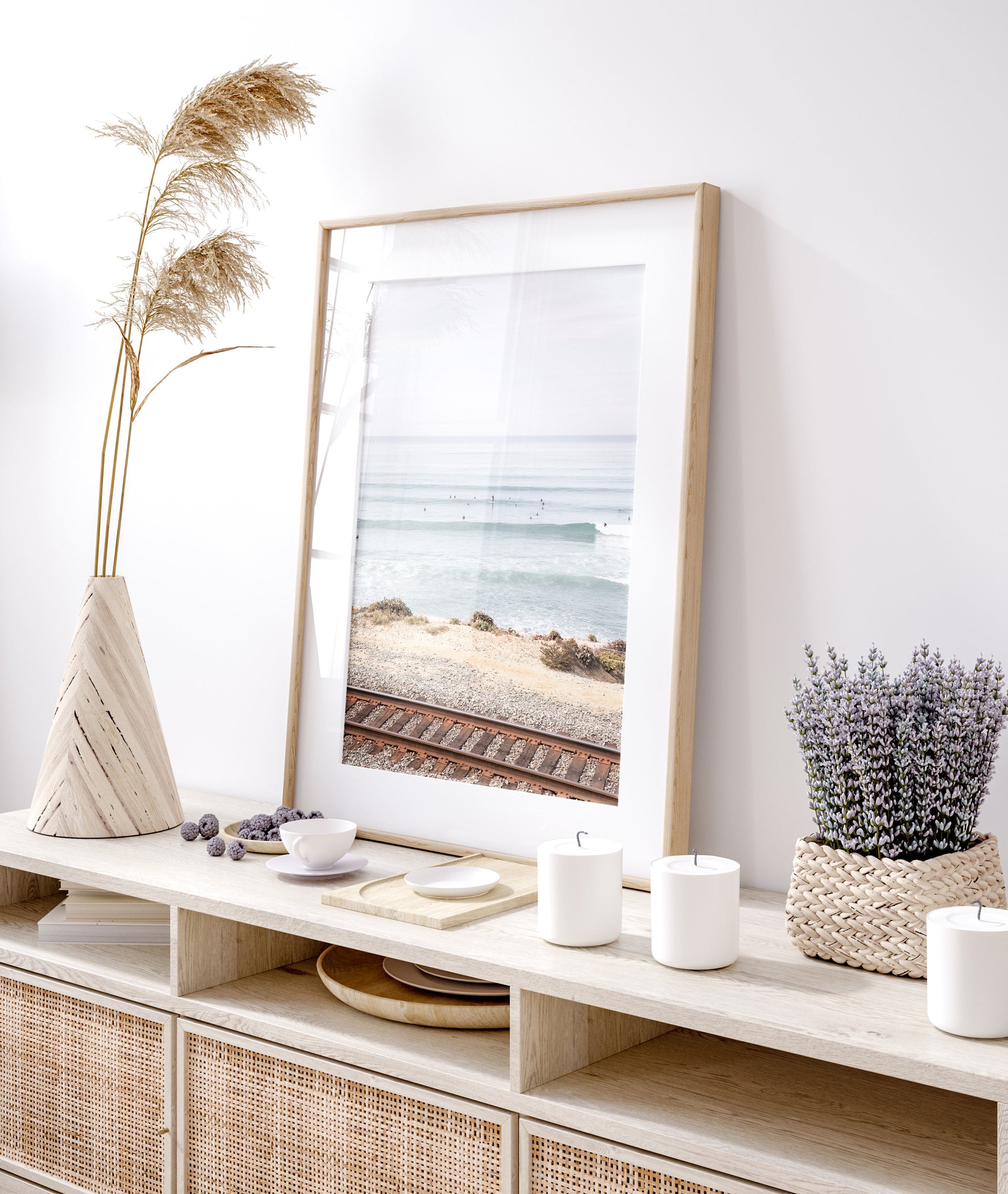 A framed print of a beach scene with waves and surfers, displayed on a train track in Del Mar, San Diego. Photograph in minimalist mock up.
