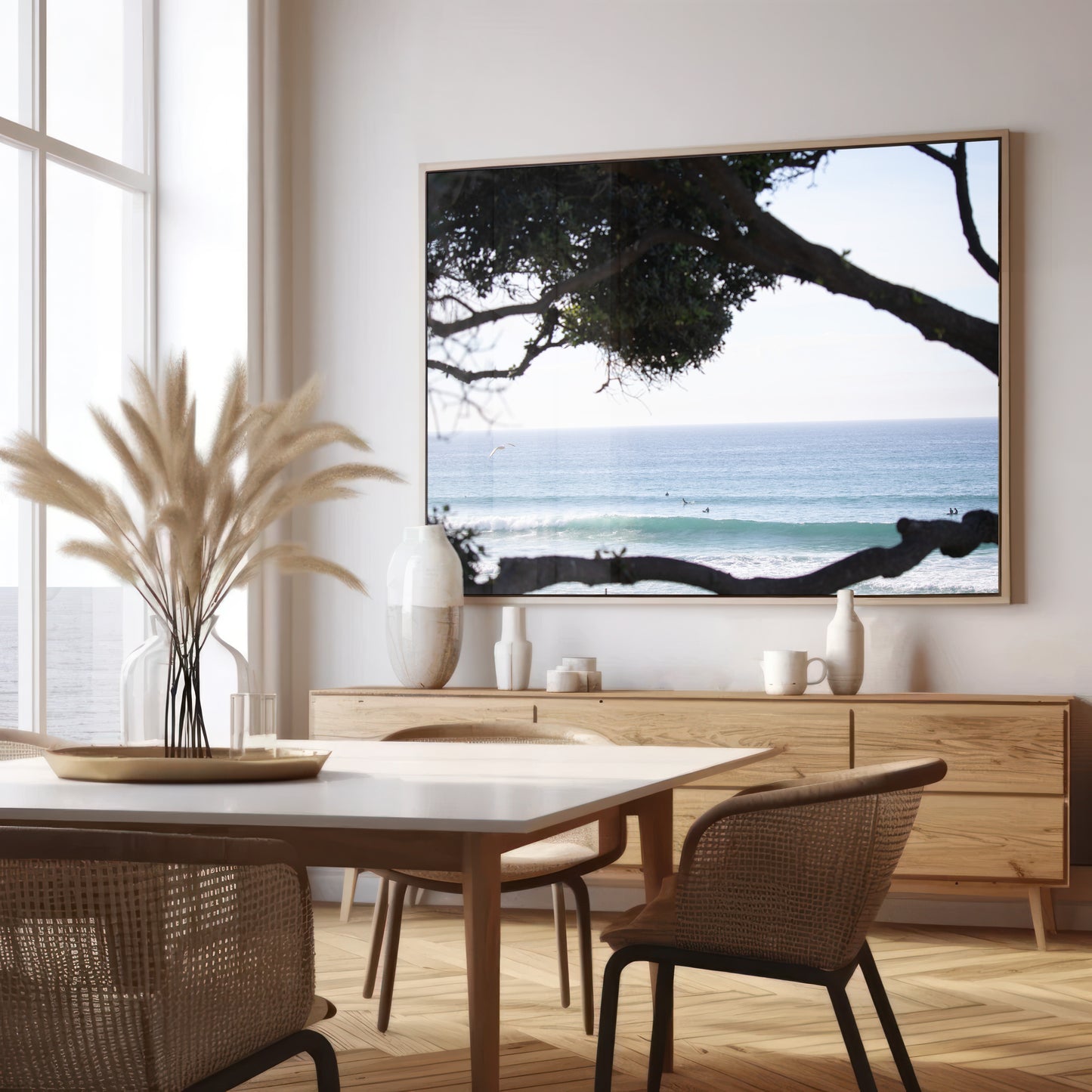An ocean view reveals surfers on gentle waves, with a white bird soaring. Tree branches provide a natural, rustic foreground to the serene scene, taken at a beach in Del Mar, San Diego. Photograph in minimalist mock up.