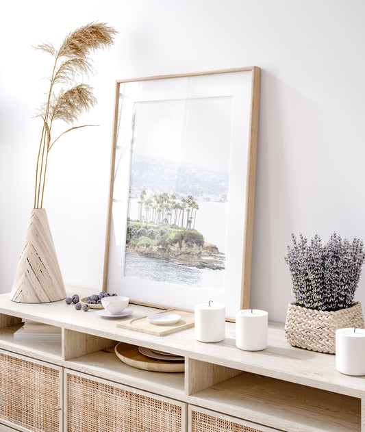 Vertical coastal photography of Laguna Beach, San Diego, featuring a fine art giclee print featuring palm trees on a small island in a body of water. Photograph in minimalist mock up.
