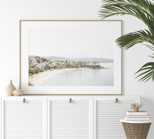 Horizontal coastal photography featuring a beach scene with a calm ocean and beach homes lining the shoreline, located in Laguna California. Photograph in minimalist mock up.