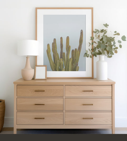 Vertical minimalist art print of a striking green cactus against a plain pale blue sky background, offering a unique element for tropical decor or minimalist art. Photograph in minimalist mock up.