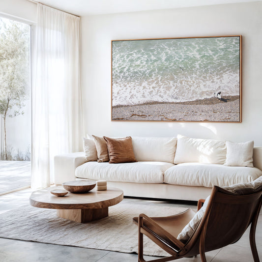 Horizontal surf print of a surfer with a surfboard walking along a rocky beach next to foamy ocean waves. This surfing art captures a unique coastline. Photograph in minimalist mock up.