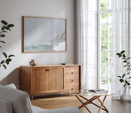 Neutral ocean print featuring a beautifully captured turquoise wave cresting with white seafoam, embodying minimalist surf art. This horizontal coastal photography showcases soft, pastel tones under a hazy sky. In the background, a rugged cliffside staircase on the right meets the sea, with faint distant surfers in the water, suggesting the expansive Southern California coastline. A tranquil piece of surf wall art, perfect for a coastal theme. Photograph in living room minimalist mock up.