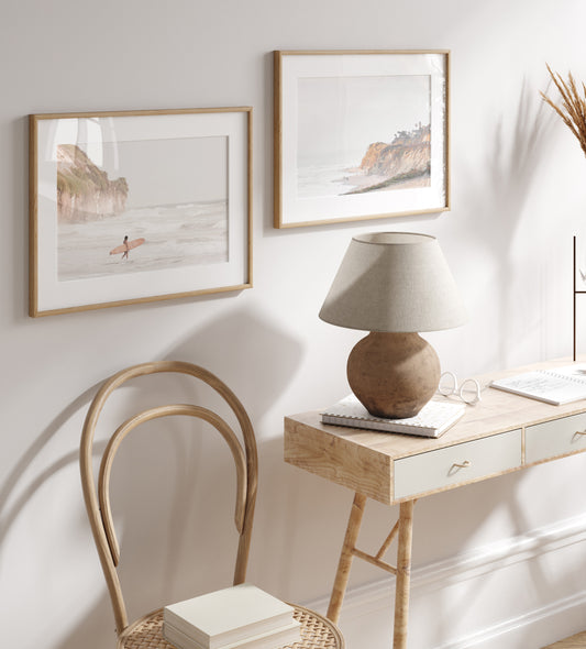 Fine art of Torrey Pines, San Diego California horizontal print of hazy high-angle landscape beach photography captures a light blue ocean meeting a sandy beach with many beach goers. To the right, tall tan and brown cliffs rise as iconic coastal scenery. Photograph in minimalist surf art mock up.