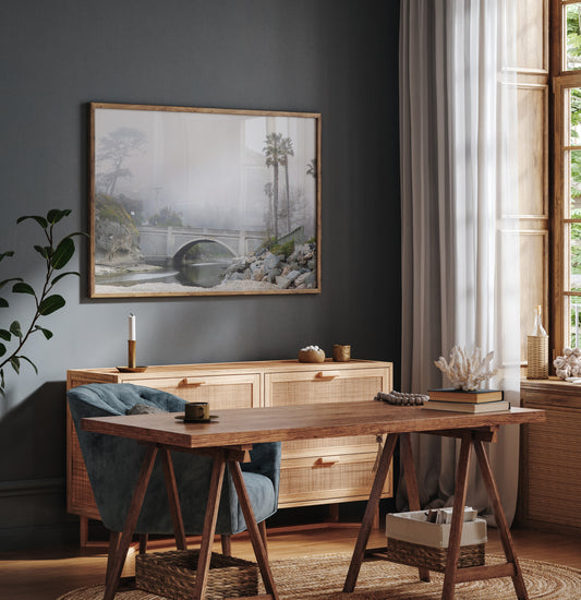 Landscape coastal photography of a concrete arch bridge disappearing into a dense fog, flanked by palm trees and rocky shores. This calm beach print evokes a mysterious seascape. Photograph in minimalist mock up.