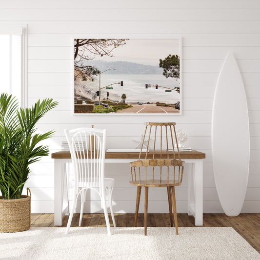 A hazy eye-level shot of San Diego Streets looks down a sloping road featuring red traffic lights and "Carmel Valley" signs, capturing a Local Surf Print vibe. The foreground of this California Wall Art showcases landscape and cars, framed by tree branches at the top, adding to the San Diego Photo aesthetic. The lighting suggests a hazy daytime, perfect for Minimalist Beach Wall Art. This horizontal San Diego print makes a great piece of horizontal beach wall decor. Photograph in minimalist mock up