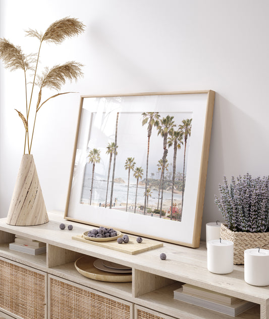 Horizontal coastal photography of a beachscape at Laguna Beach, California, beach art print featuring palm trees and a clear blue sky with a few clouds over a beach scene. Photograph in minimalist mock up.