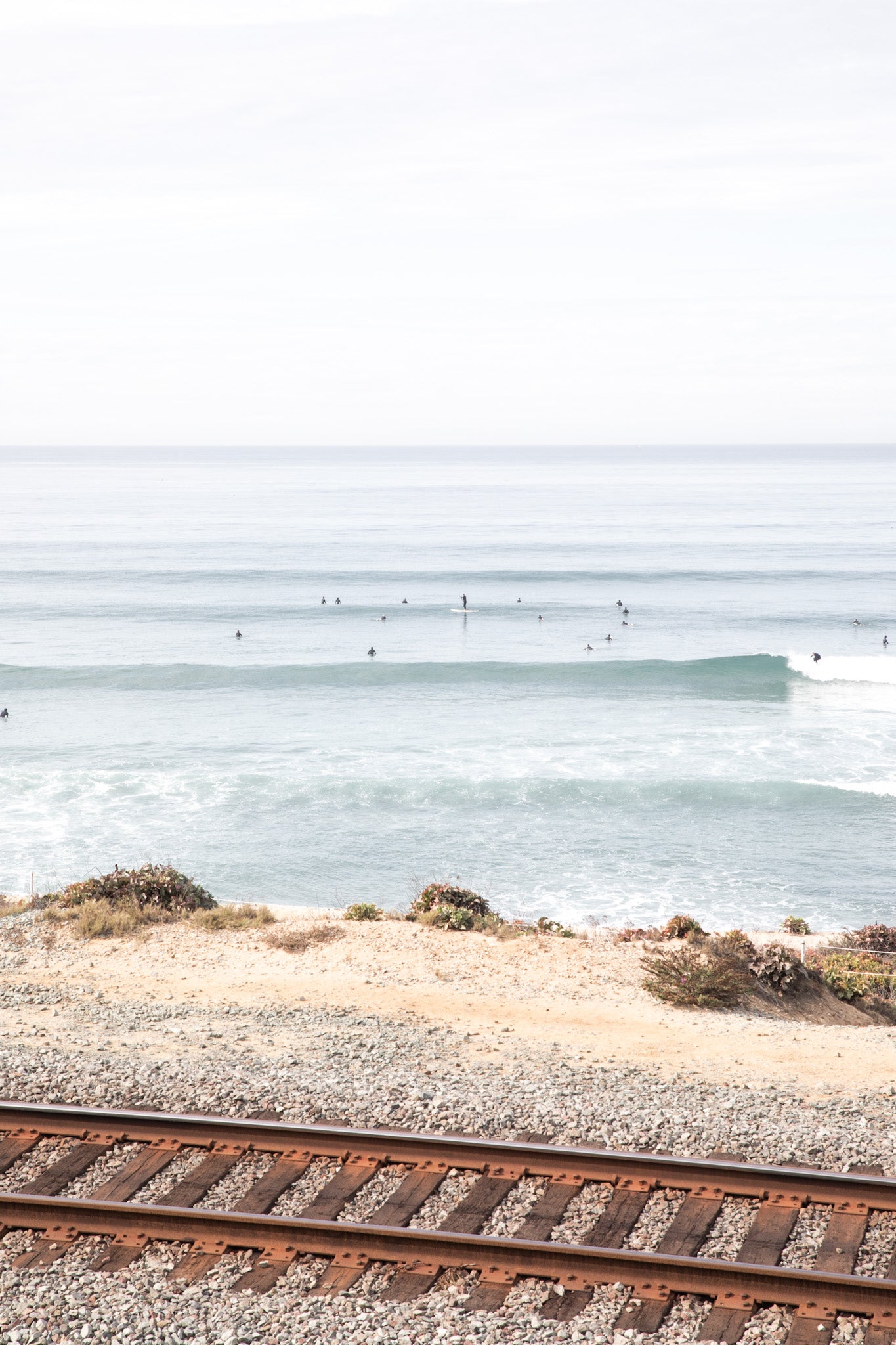 A framed print of a beach scene with waves and surfers, displayed on a train track in Del Mar, San Diego.