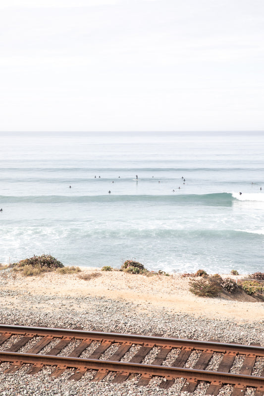 A framed print of a beach scene with waves and surfers, displayed on a train track in Del Mar, San Diego.