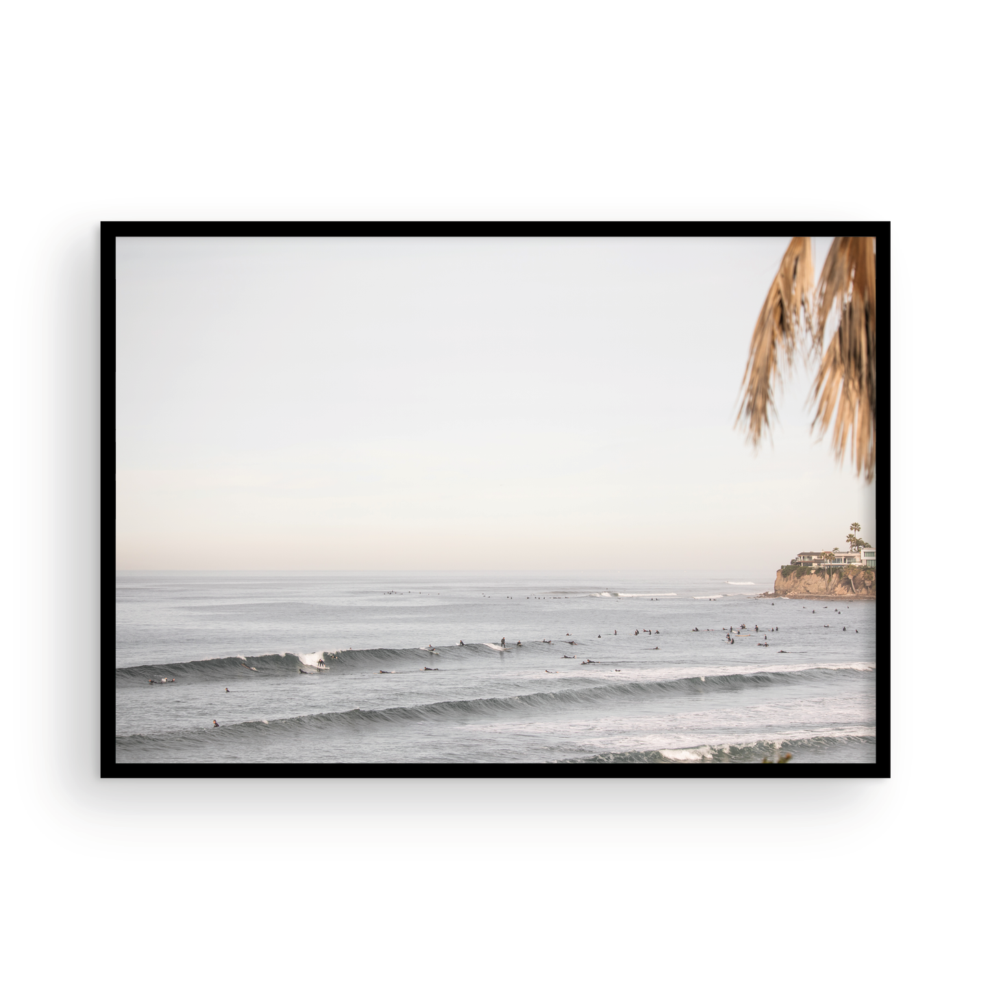 Landscape beach photography of Tourmaline Beach, Pacific Beach, California, with waves and many surfers, framed by a palm tree in the corner. This ocean print captures casual surf vibes. Photograph in minimalist mock up.