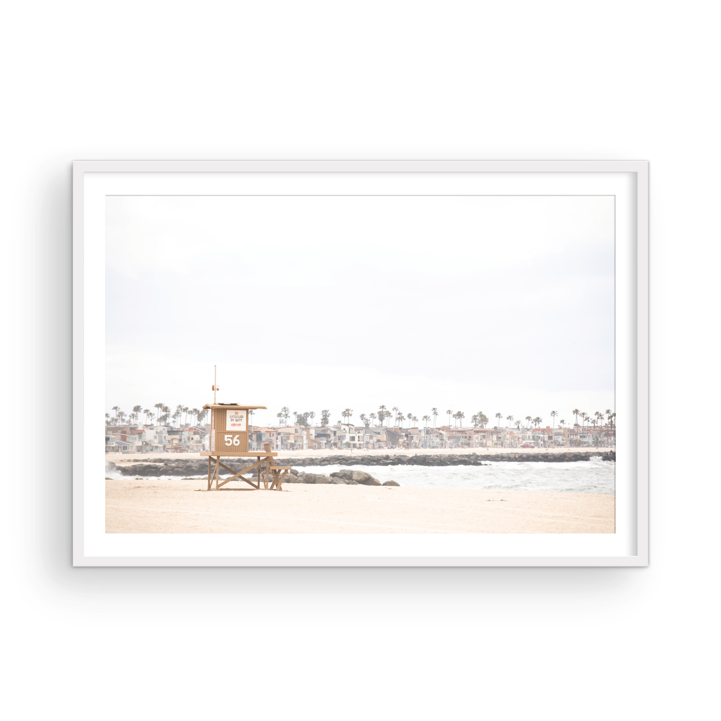 Landscape beach photography of Newport Beach, featuring lifeguard tower 56 on the sand with ocean waves and coastal houses in the background. A great Newport Beach photography print. Photograph in minimalist mock up