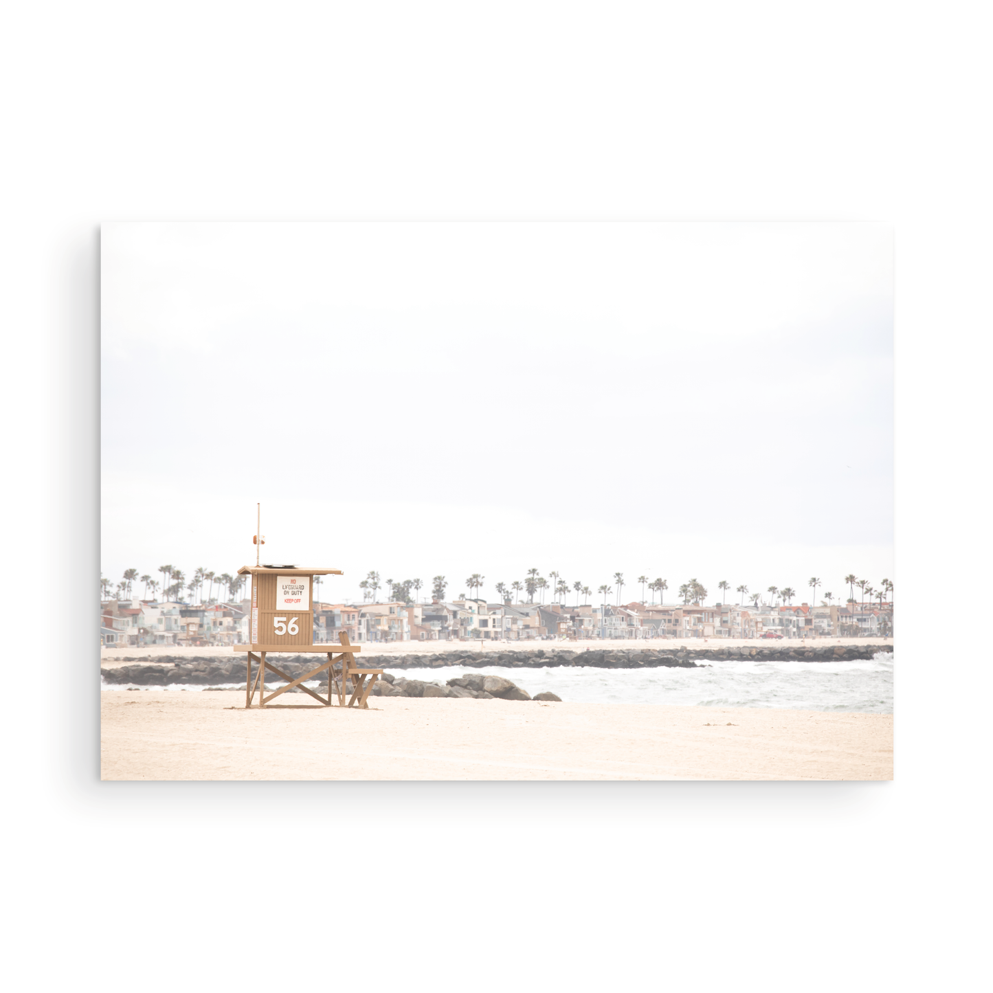 Landscape beach photography of Newport Beach, featuring lifeguard tower 56 on the sand with ocean waves and coastal houses in the background. A great Newport Beach photography print. Photograph in minimalist mock up