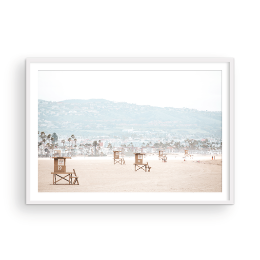 Landscape beach photography of Santa Monica State Beach with multiple lifeguard towers on the vast sandy expanse and hazy hills in the background. Photograph in minimalist mock up