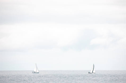 Minimalist ocean print featuring two sailboats on a calm ocean under a vast, bright sky. This serene seascape is ideal for coastal, nautical theme wall art. Photograph in minimalist mock up