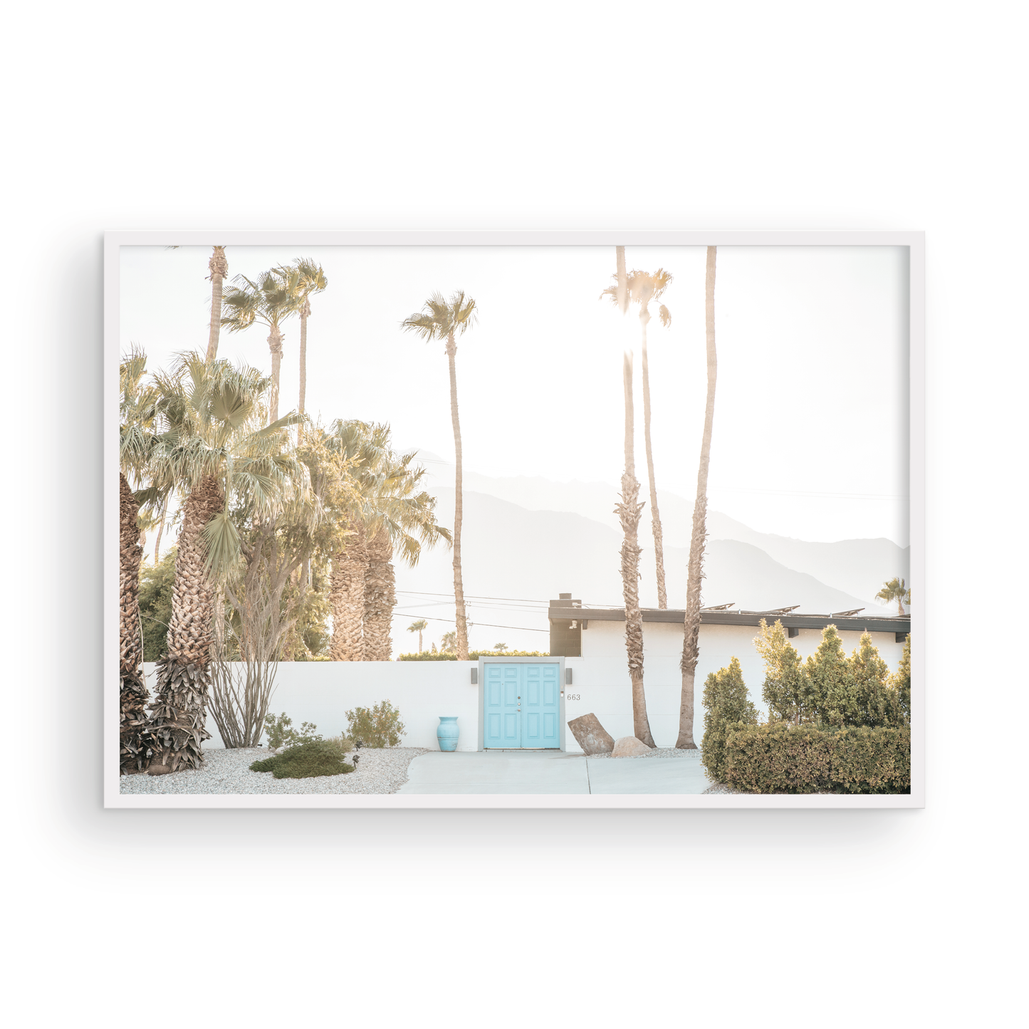 Coastal print of a Palm Springs home with a bright blue door, surrounded by tall palm trees and distant mountains, embodying summer vibes wall art. Photograph in minimalist mock up.