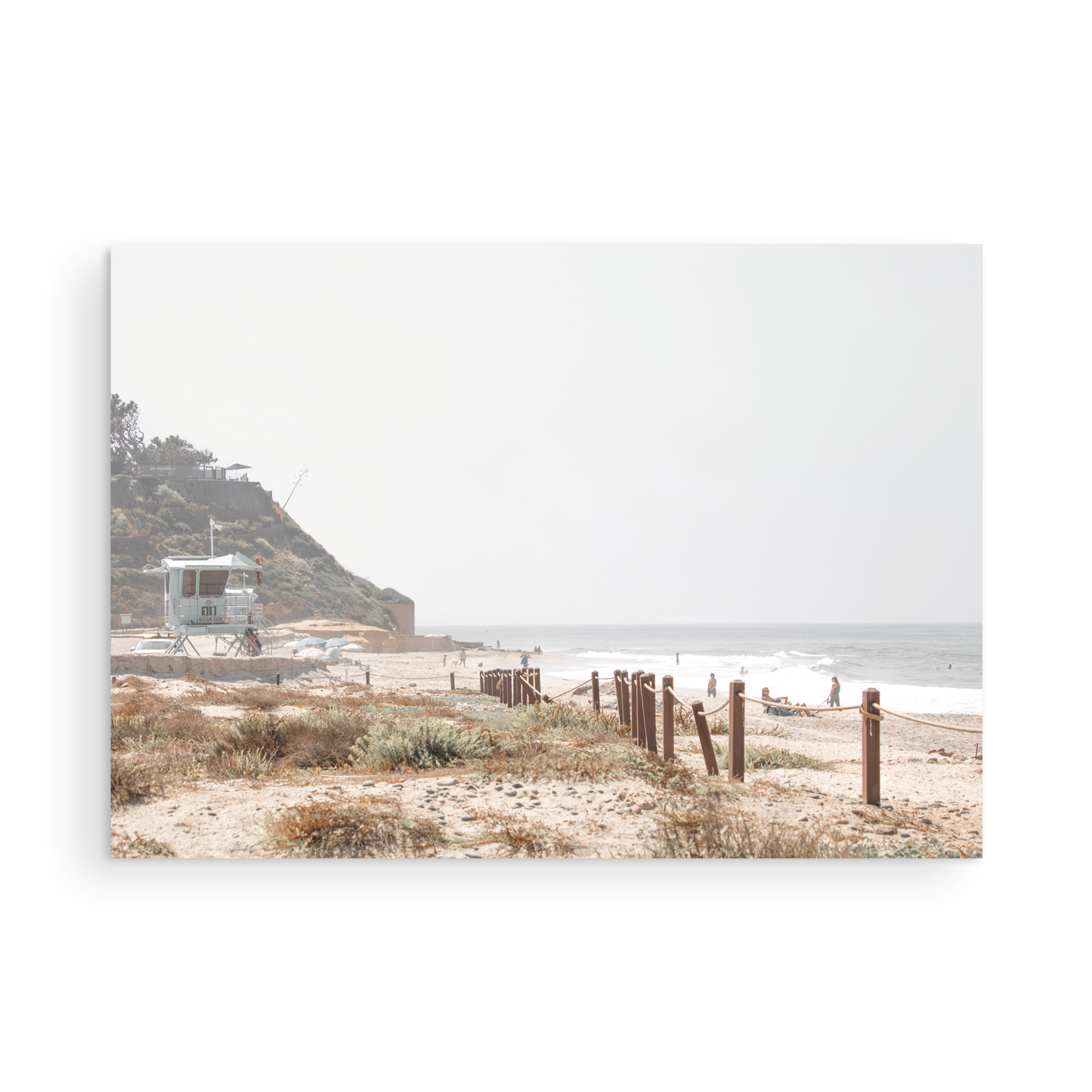 Landscape coastal photography of a light-colored lifeguard tower at a Southern California beach, with a rustic wooden fence leading towards the ocean waves. This tranquil beachscape print is ideal for beach cottage wall decor or a calm beach print. Photograph in minimalist mock up.