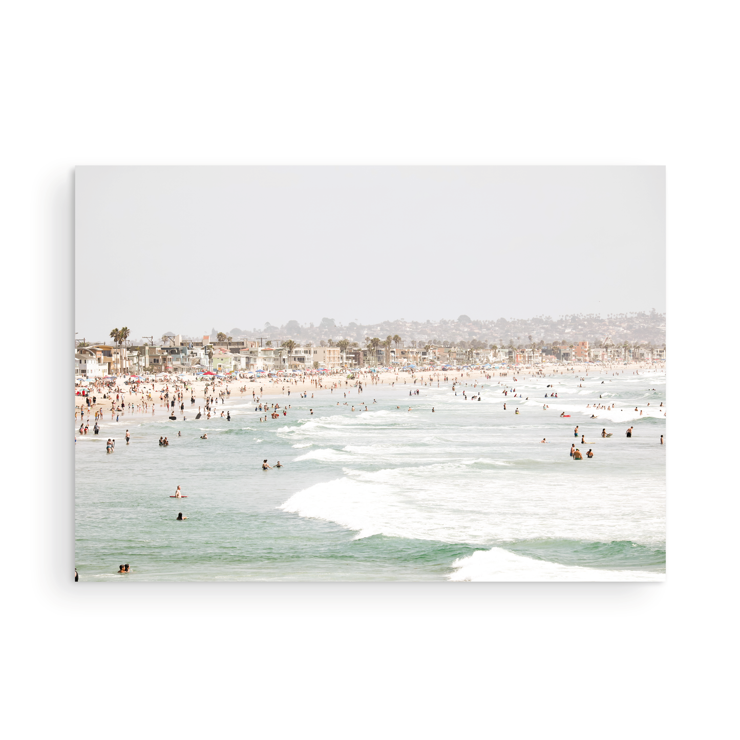 Landscape beach photography of a busy San Diego public beach with many people in the sand and ocean waves, a true summer vibes scene. Photograph in minimalist mock up.