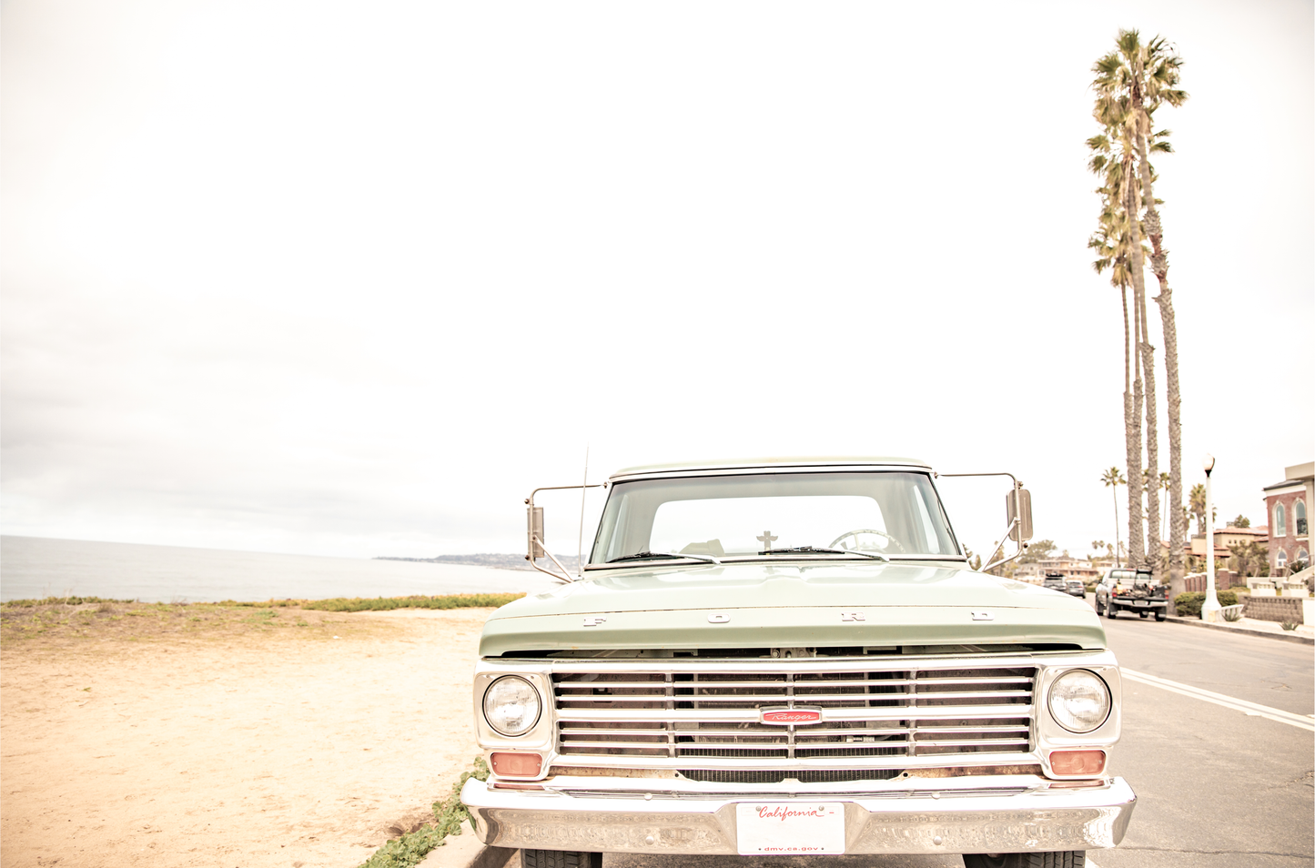 Nostalgic Southern California beach art featuring a classic light green Ford F-Series pickup truck parked by the San Diego coast. This horizontal surf print captures the vintage vehicle with a backdrop of iconic tall palm trees, a hazy beach, and the ocean, embodying surf vibes and perfect for coastal farmhouse decor.