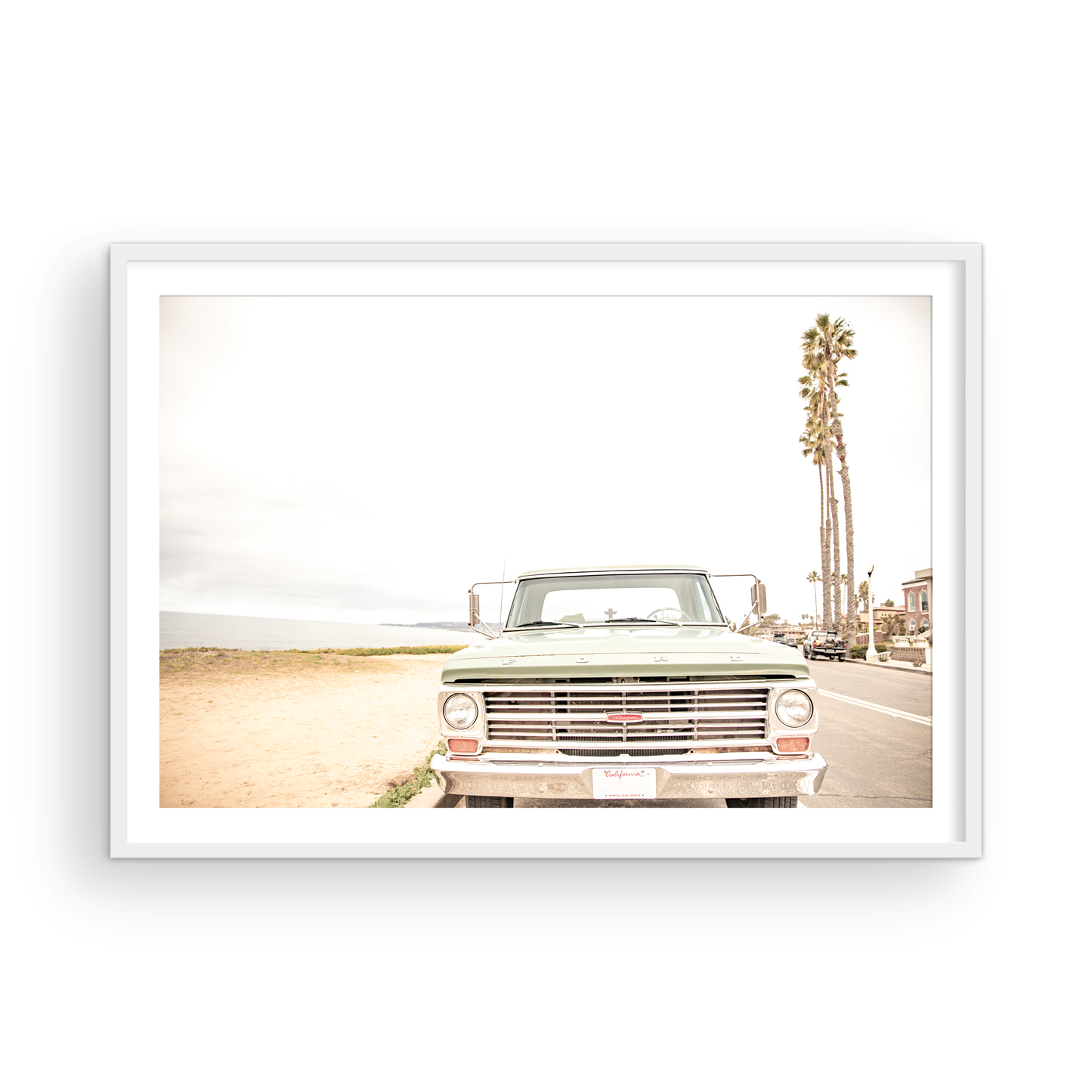 Nostalgic Southern California beach art featuring a classic light green Ford F-Series pickup truck parked by the San Diego coast. This horizontal surf print captures the vintage vehicle with a backdrop of iconic tall palm trees, a hazy beach, and the ocean, embodying surf vibes and perfect for coastal farmhouse decor. Photograph in minimalist framed mock up.