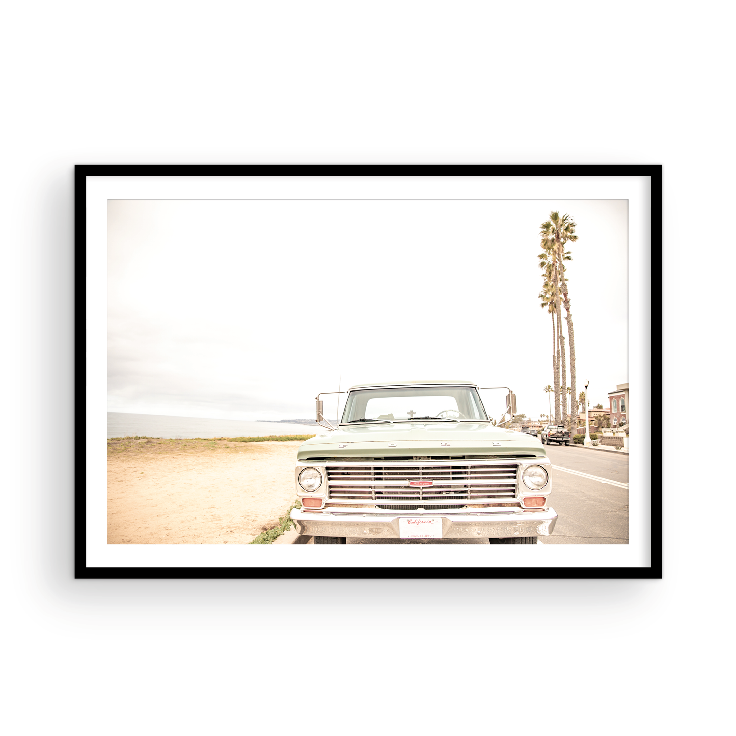 Nostalgic Southern California beach art featuring a classic light green Ford F-Series pickup truck parked by the San Diego coast. This horizontal surf print captures the vintage vehicle with a backdrop of iconic tall palm trees, a hazy beach, and the ocean, embodying surf vibes and perfect for coastal farmhouse decor. Photograph in minimalist framed mock up.