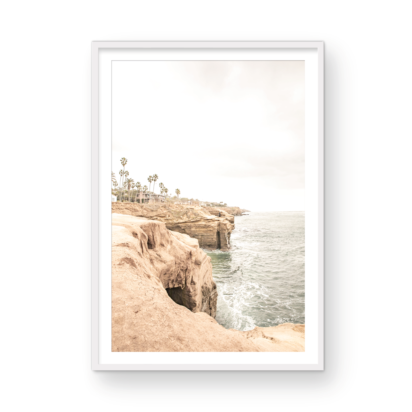 Fine art of Sunset Cliffs, San Diego California vertical print of hazy high-angle landscape beach photography captures a light blue ocean meeting tall tan, brown cliffs rise as iconic coastal scenery. Photograph in minimalist mock up.