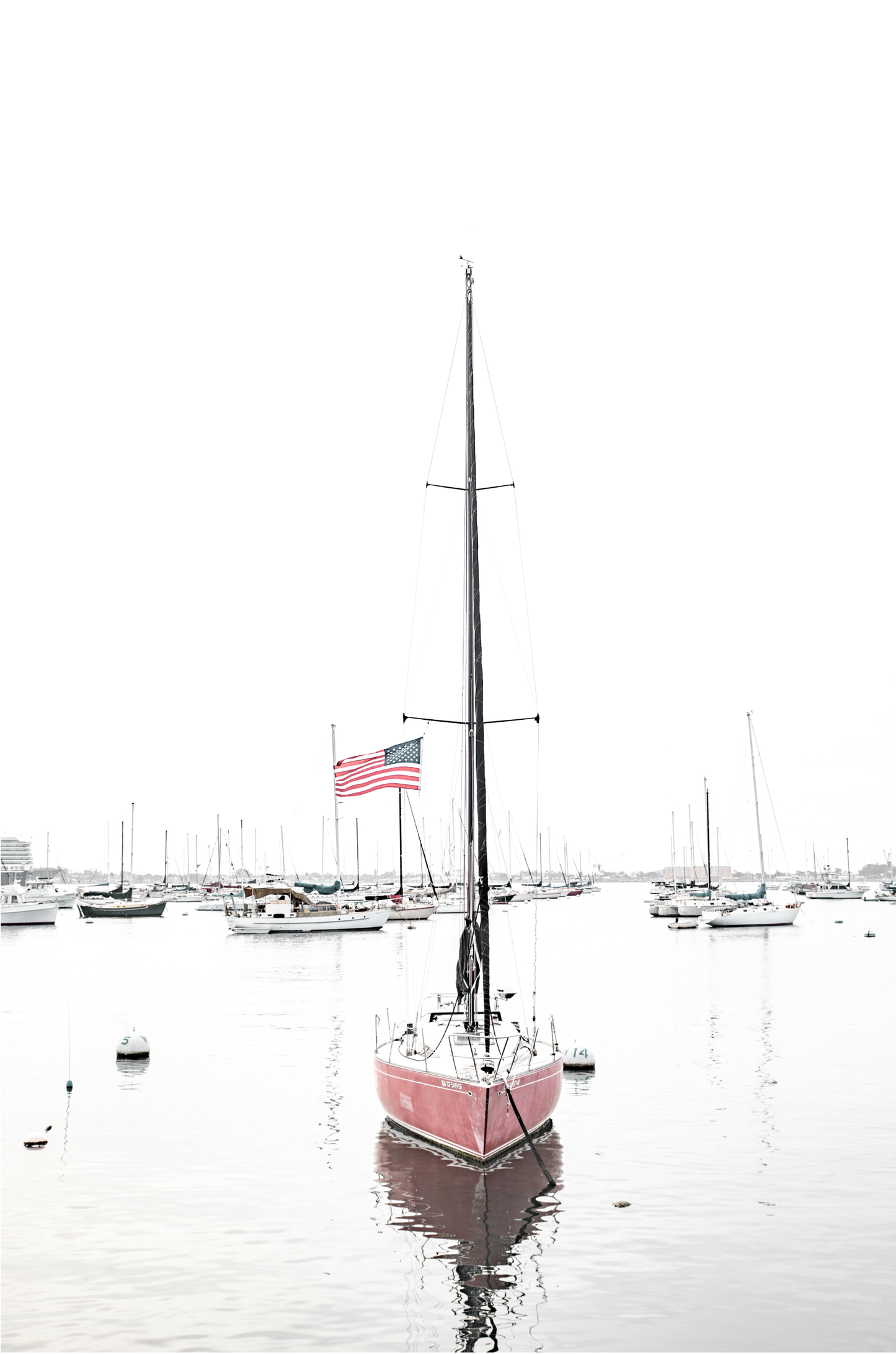 A vertical San Diego print featuring a lone red sailboat with an American flag, anchored in a calm San Diego harbor. This minimalist ocean print captures the essence of coastal photography and is perfect for modern coastal decor.