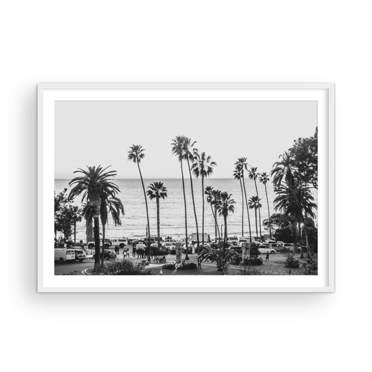 A classic black and white horizontal print of Swamis, the iconic San Diego surf spot, showcasing a panoramic view from above. This piece of Southern California travel photography features dozens of silhouetted palm trees against a bright sky, with a lively beach scene of cars and people below, stretching towards the ocean. Perfect as timeless beach art or neutral coastal decor for a surf vibe. Photograph in minimalist framed mock up.