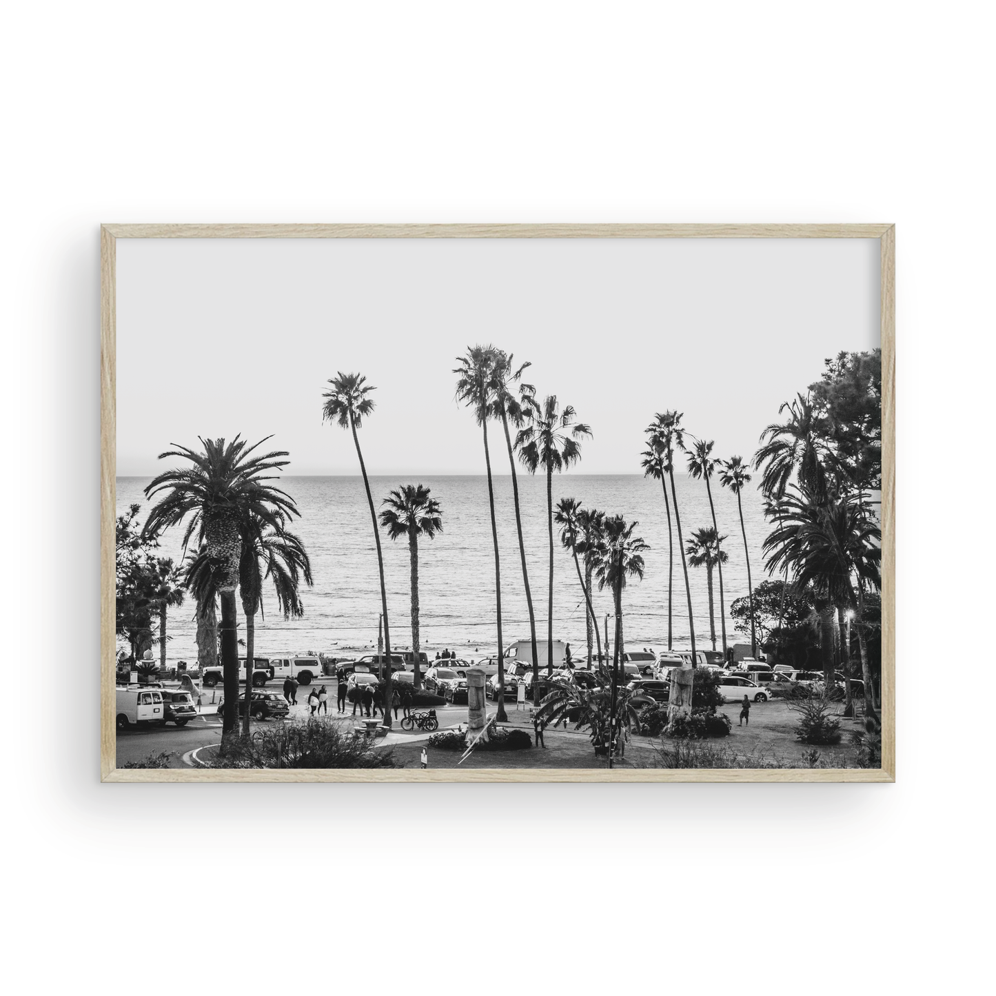 A classic black and white horizontal print of Swamis, the iconic San Diego surf spot, showcasing a panoramic view from above. This piece of Southern California travel photography features dozens of silhouetted palm trees against a bright sky, with a lively beach scene of cars and people below, stretching towards the ocean. Perfect as timeless beach art or neutral coastal decor for a surf vibe. Photograph in minimalist framed mock up.