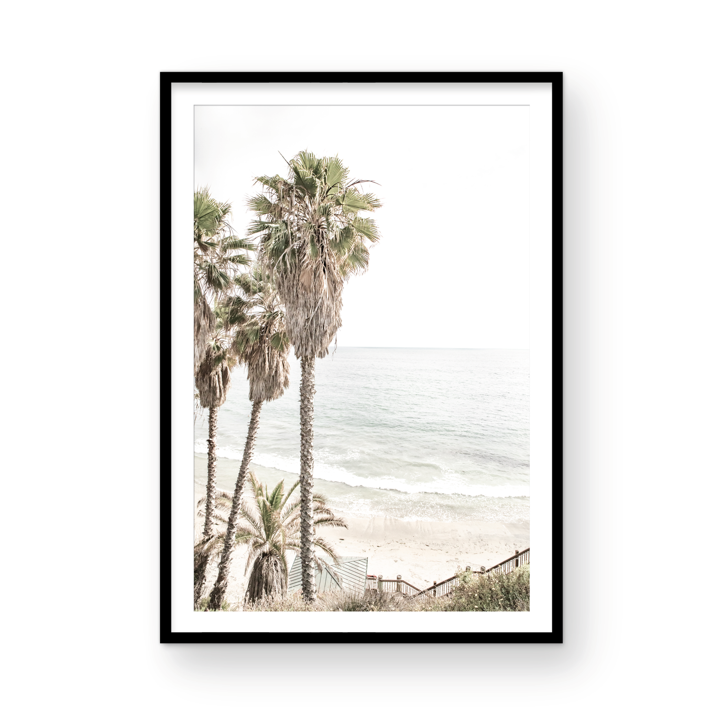 Dreamy coastal palm tree print featuring several tall palm trees with shaggy trunks, next to a staircase down to a tranquil beach. This vertical tropical print is captured at Swamis Beach on the Southern California coast, is bathed in bright, hazy sunlight, creating a pastel beach art effect. Evokes serene summer vibes, perfect for beach house decor. Photograph in minimalist surf art mock up.