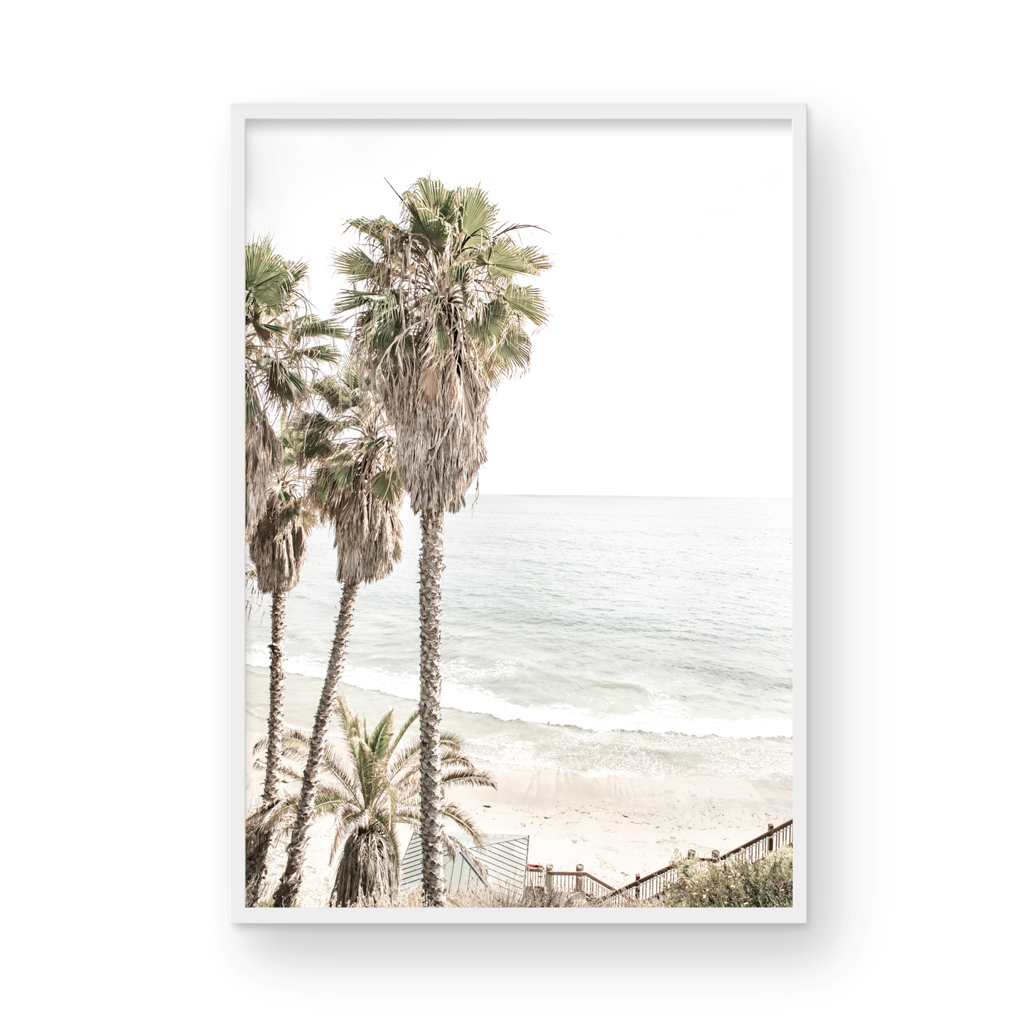 Dreamy coastal palm tree print featuring several tall palm trees with shaggy trunks, next to a staircase down to a tranquil beach. This vertical tropical print is captured at Swamis Beach on the Southern California coast, is bathed in bright, hazy sunlight, creating a pastel beach art effect. Evokes serene summer vibes, perfect for beach house decor. Photograph in minimalist surf art mock up.