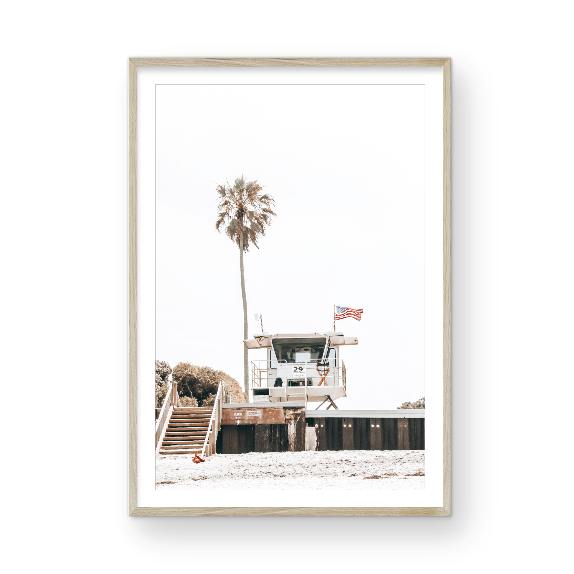 A photograph featuring an American flag on a lifeguard tower with a palm tree in the background, taken at a beach in Del Mar, San Diego. Photograph in minimalist mock up.