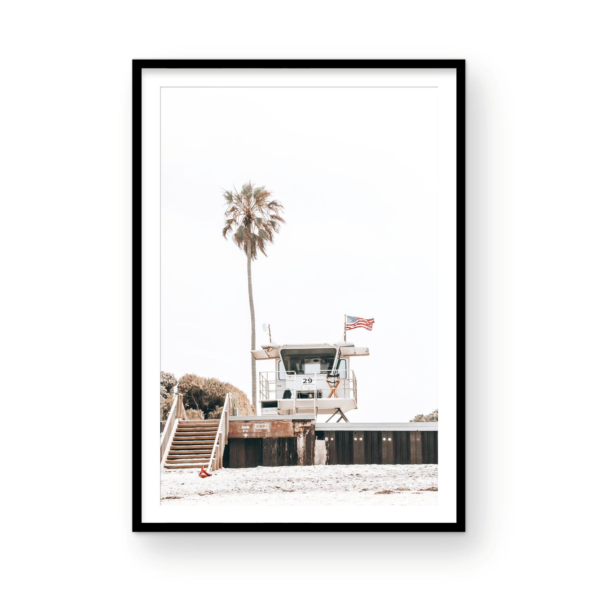 A photograph featuring an American flag on a lifeguard tower with a palm tree in the background, taken at a beach in Del Mar, San Diego. Photograph in minimalist mock up.