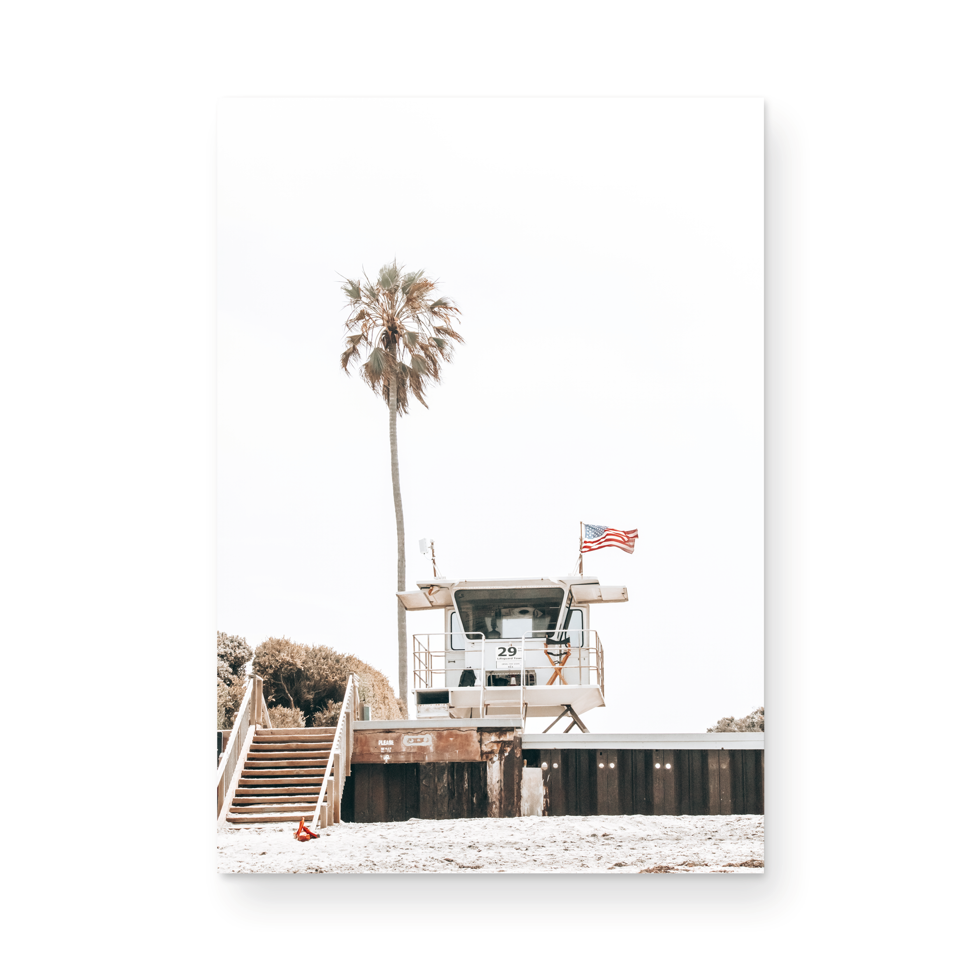 A photograph featuring an American flag on a lifeguard tower with a palm tree in the background, taken at a beach in Del Mar, San Diego. Photograph in minimalist mock up.