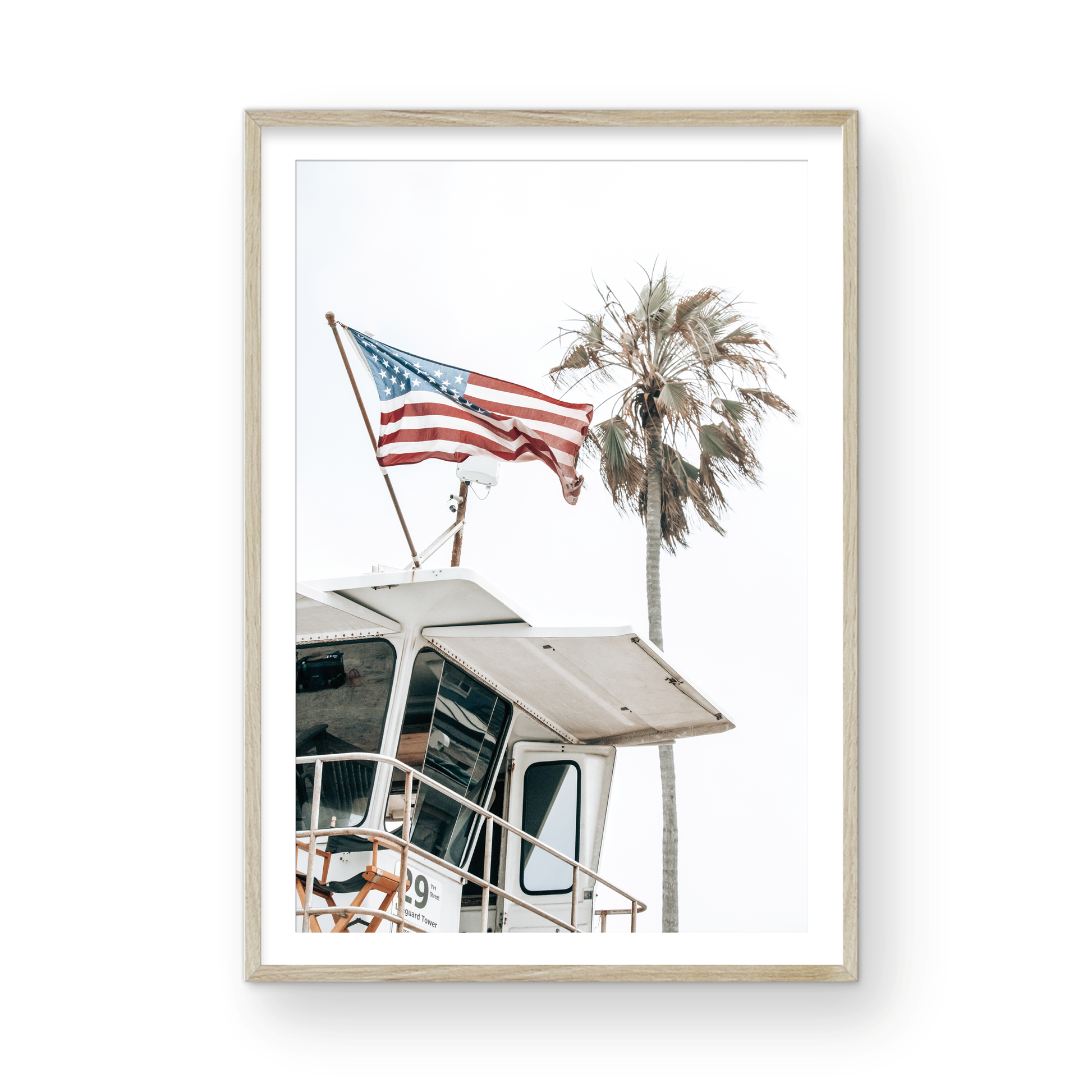An American flag attached to a lifeguard tower with palm trees in the background, captured in California with a clear sky in the top half of the image. Photograph in minimalist mock up.