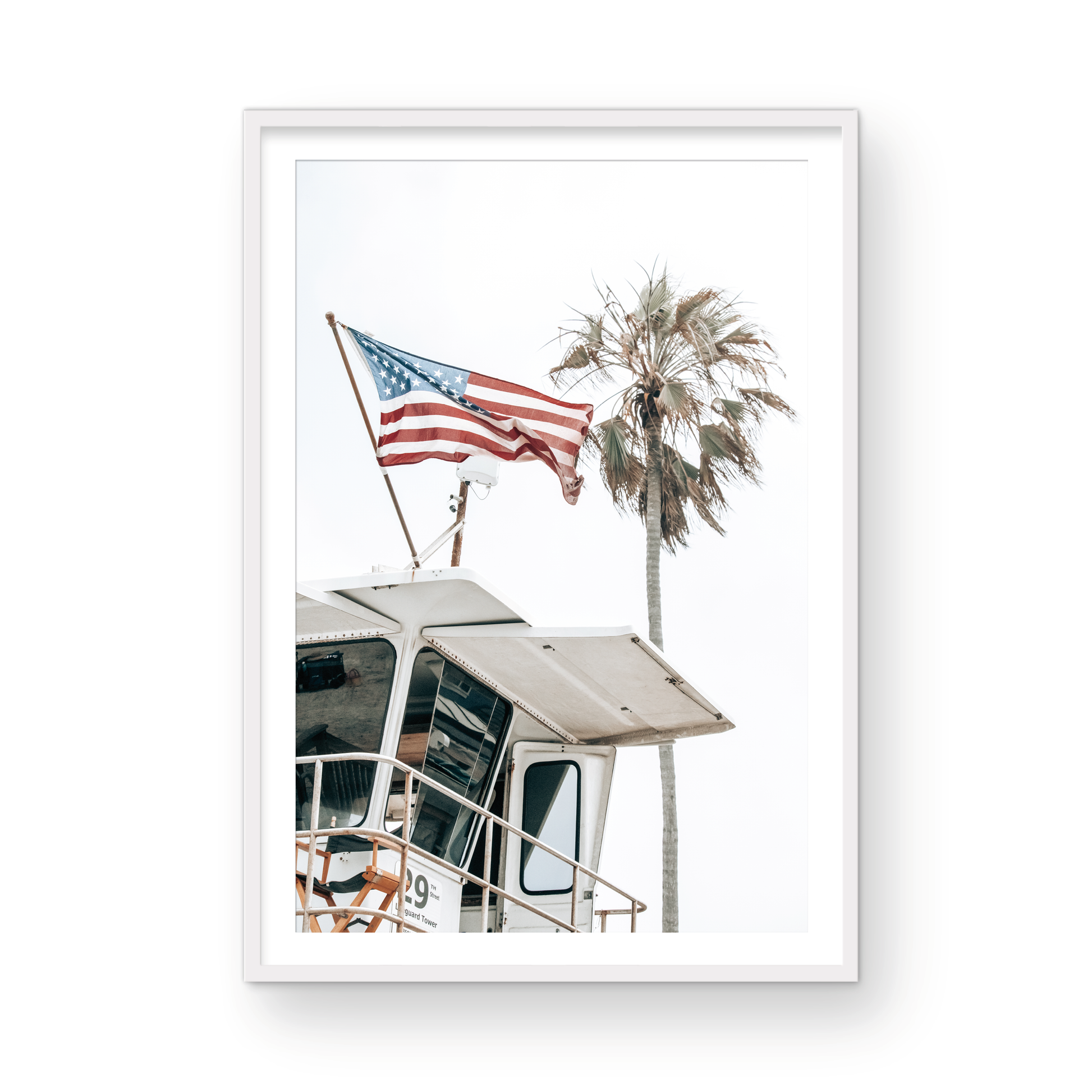 An American flag attached to a lifeguard tower with palm trees in the background, captured in California with a clear sky in the top half of the image. Photograph in minimalist mock up.
