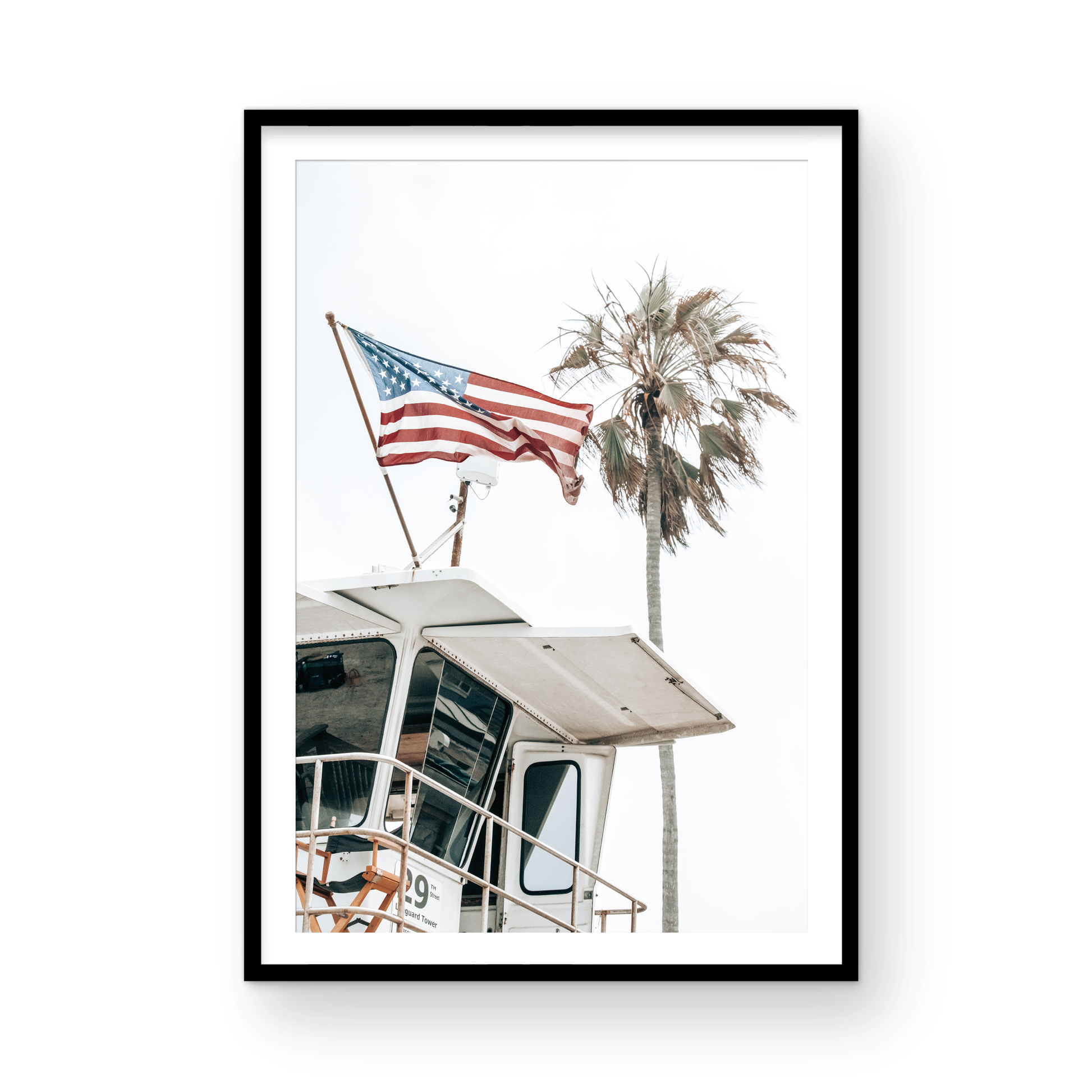 An American flag attached to a lifeguard tower with palm trees in the background, captured in California with a clear sky in the top half of the image. Photograph in minimalist mock up.