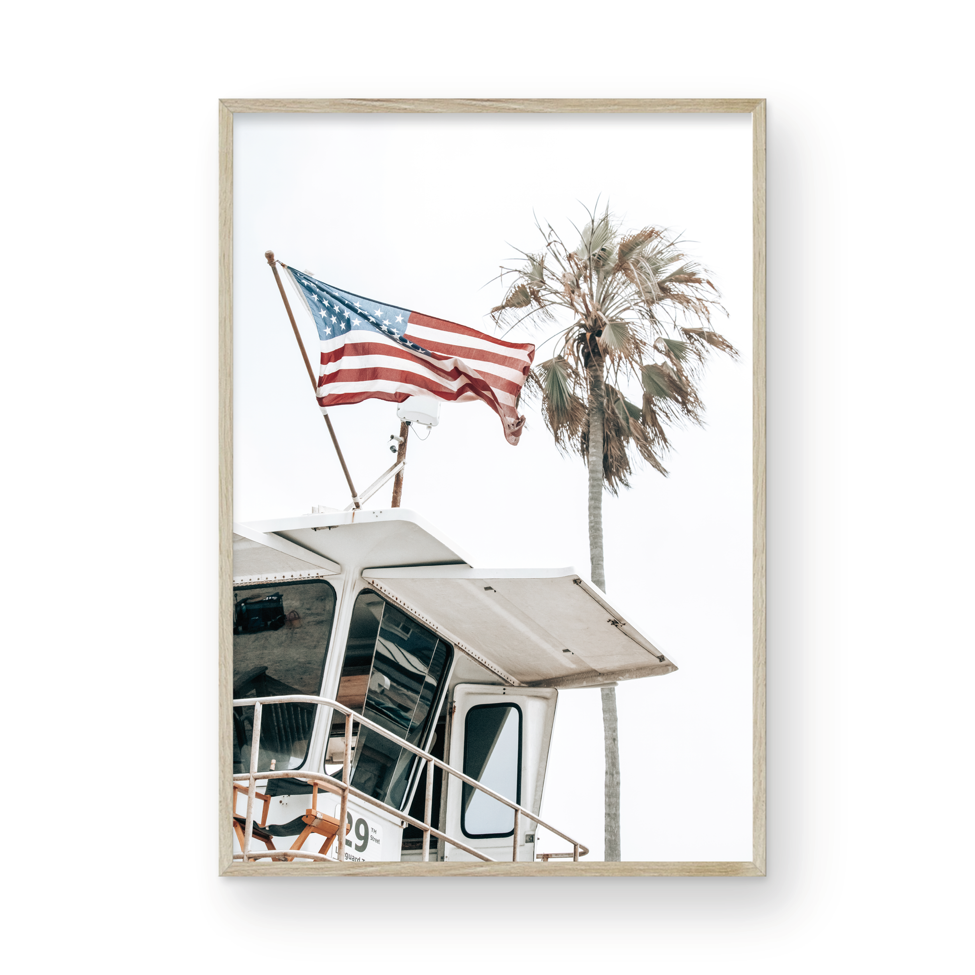 An American flag attached to a lifeguard tower with palm trees in the background, captured in California with a clear sky in the top half of the image. Photograph in minimalist mock up.