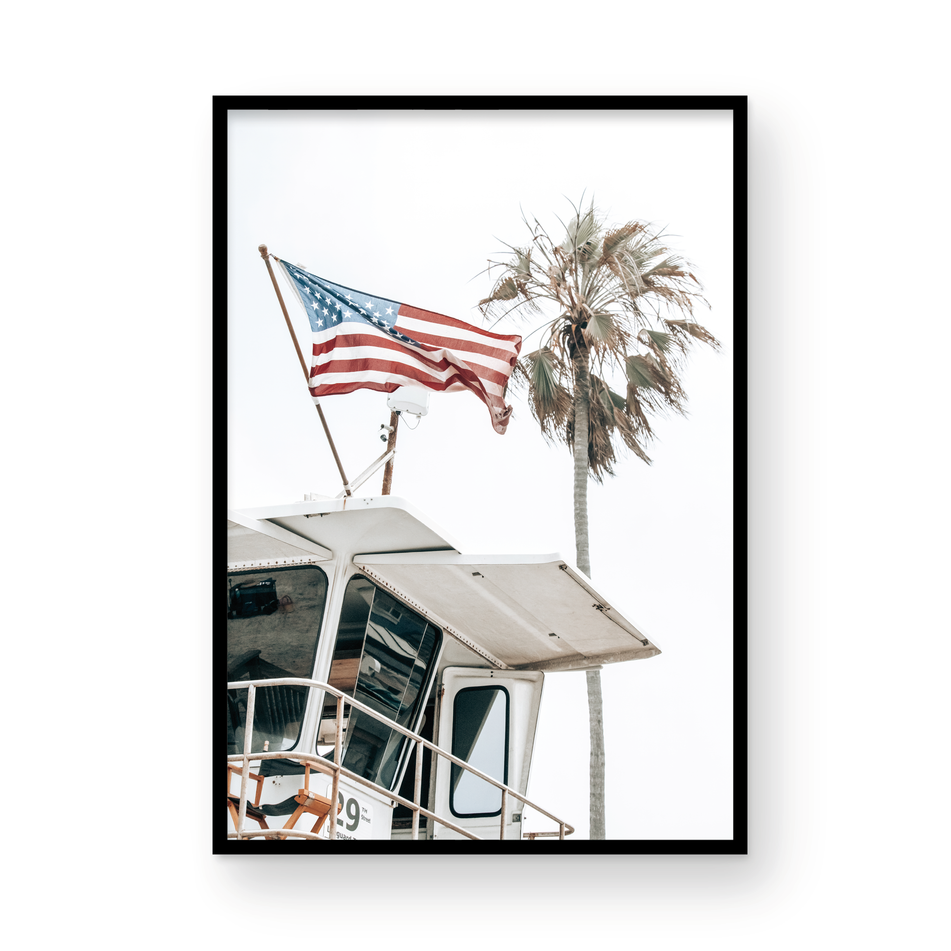 An American flag attached to a lifeguard tower with palm trees in the background, captured in California with a clear sky in the top half of the image. Photograph in minimalist mock up.