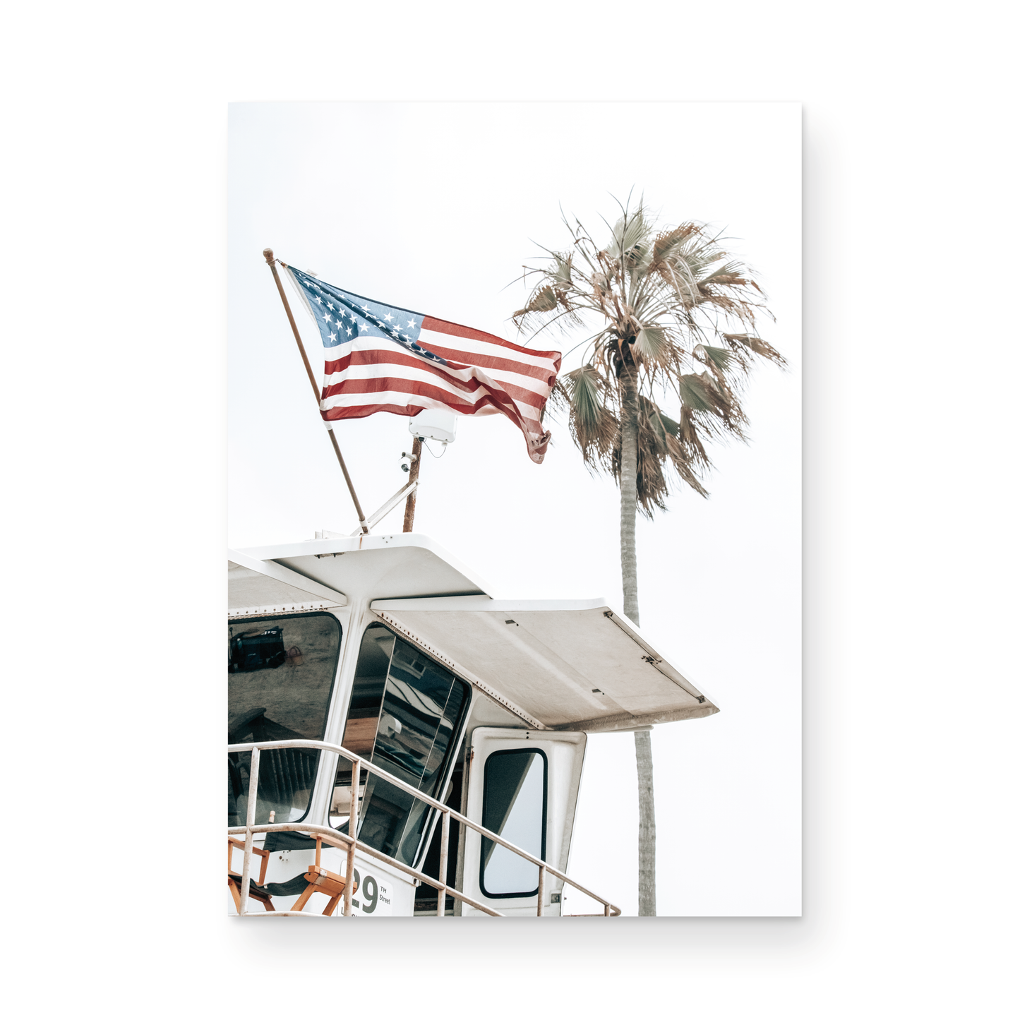 An American flag attached to a lifeguard tower with palm trees in the background, captured in California with a clear sky in the top half of the image. Photograph in minimalist mock up.