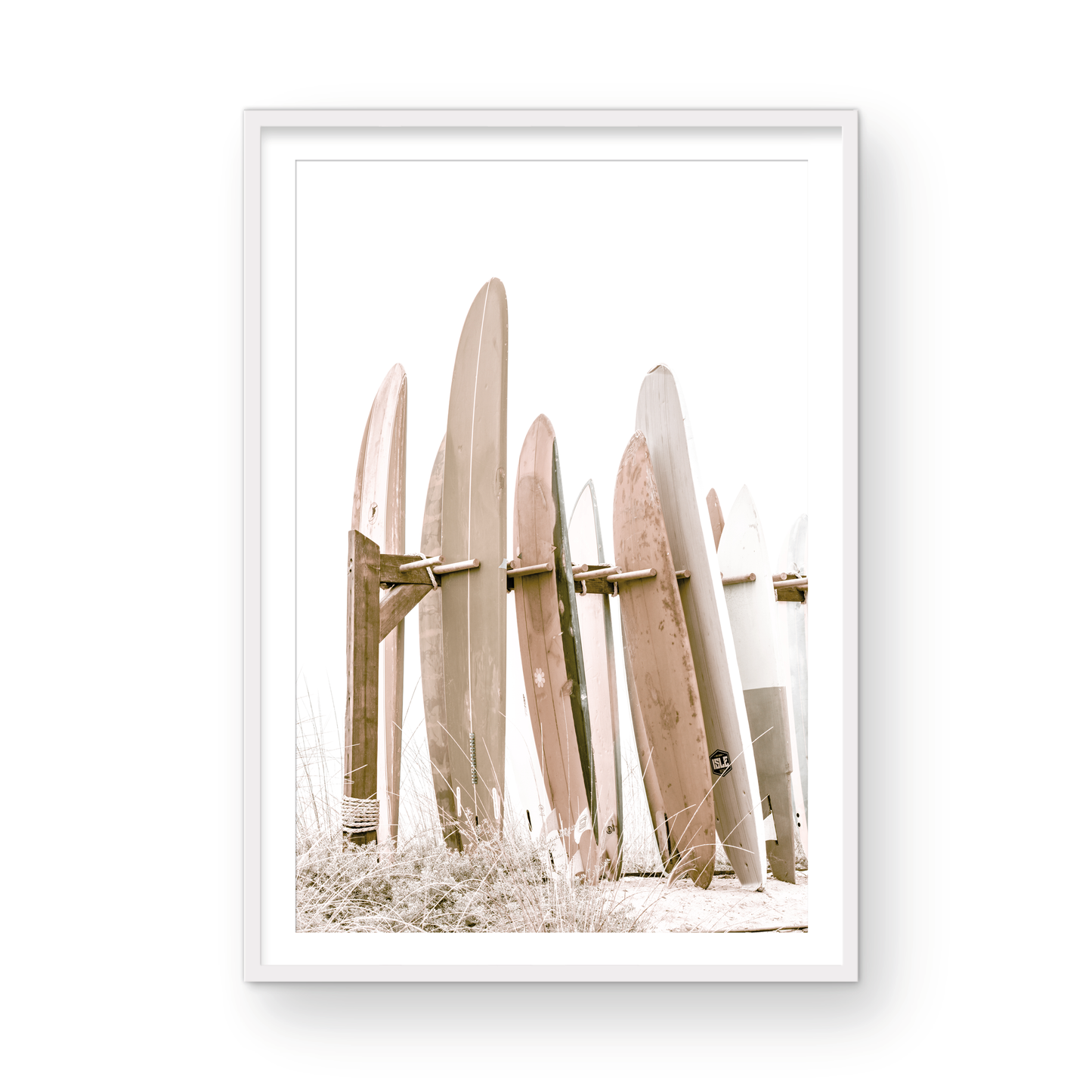 framed Neutral surfboard wall art. fine art photography for the modern coastal home. Minimalist vertical surf art print showcasing a line-up of surfboards in various lengths and soft, neutral pastel hues, resting on a simple wooden rack with some dry grass in the foreground. This piece of surf wall decor features a bright, hazy white backdrop, enhancing its clean aesthetic. Perfect as pastel surf decor or for adding surf vibes to kids surf room decor or a beach house.