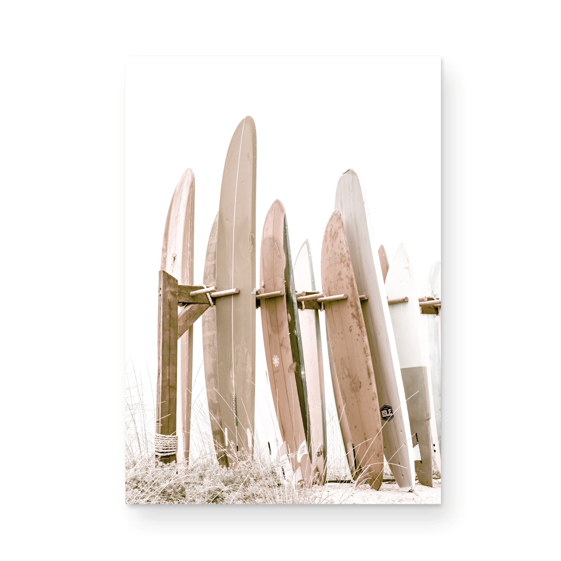Neutral surfboard wall art. fine art photography for beach house decor. Minimalist vertical surf art print showcasing a line-up of surfboards in various lengths and soft, neutral pastel hues, resting on a simple wooden rack with some dry grass in the foreground. This piece of surf wall decor features a bright, hazy white backdrop, enhancing its clean aesthetic. Perfect as pastel surf decor or for adding surf vibes to kids surf room decor or a beach house.
