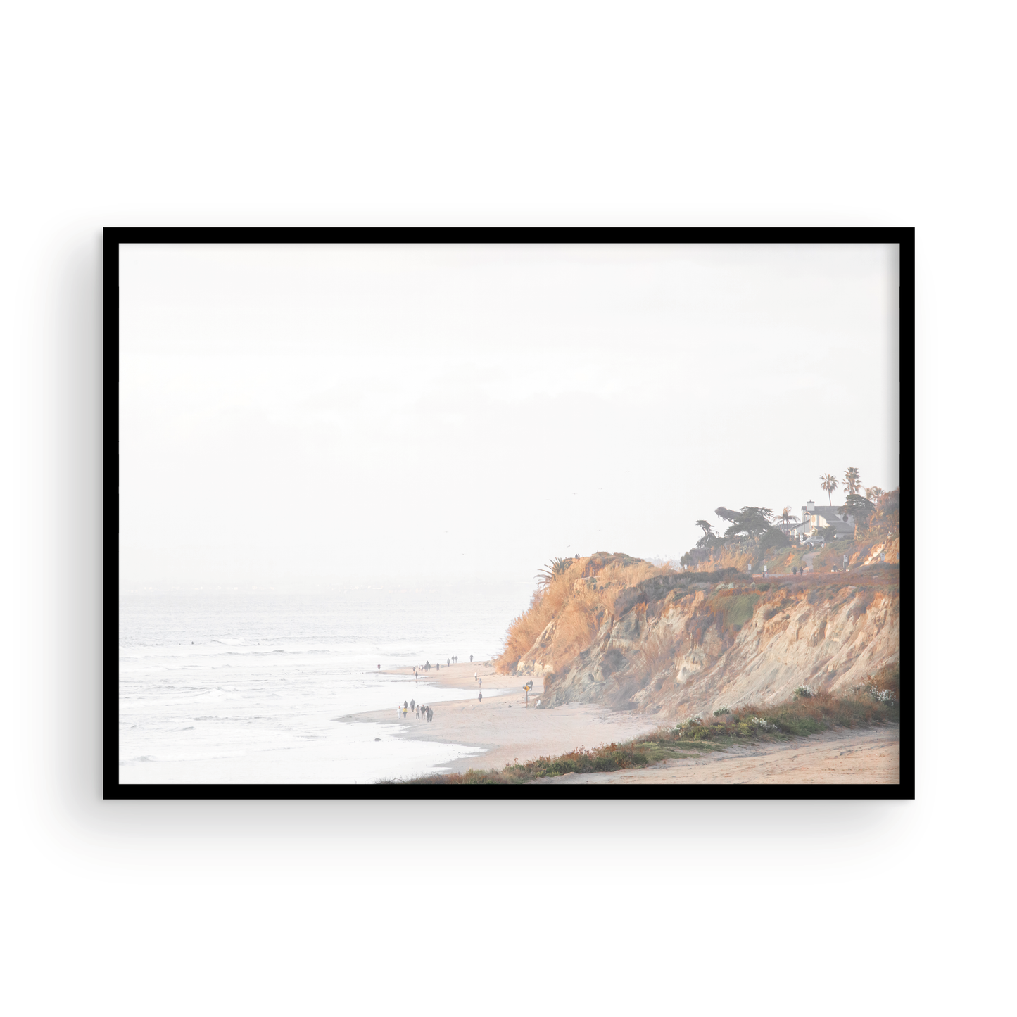 Fine art of Torrey Pines, San Diego California horizontal print of hazy high-angle landscape beach photography captures a light blue ocean meeting a sandy beach with many beach goers. To the right, tall tan and brown cliffs rise as iconic coastal scenery. Photograph in minimalist framed mock up.