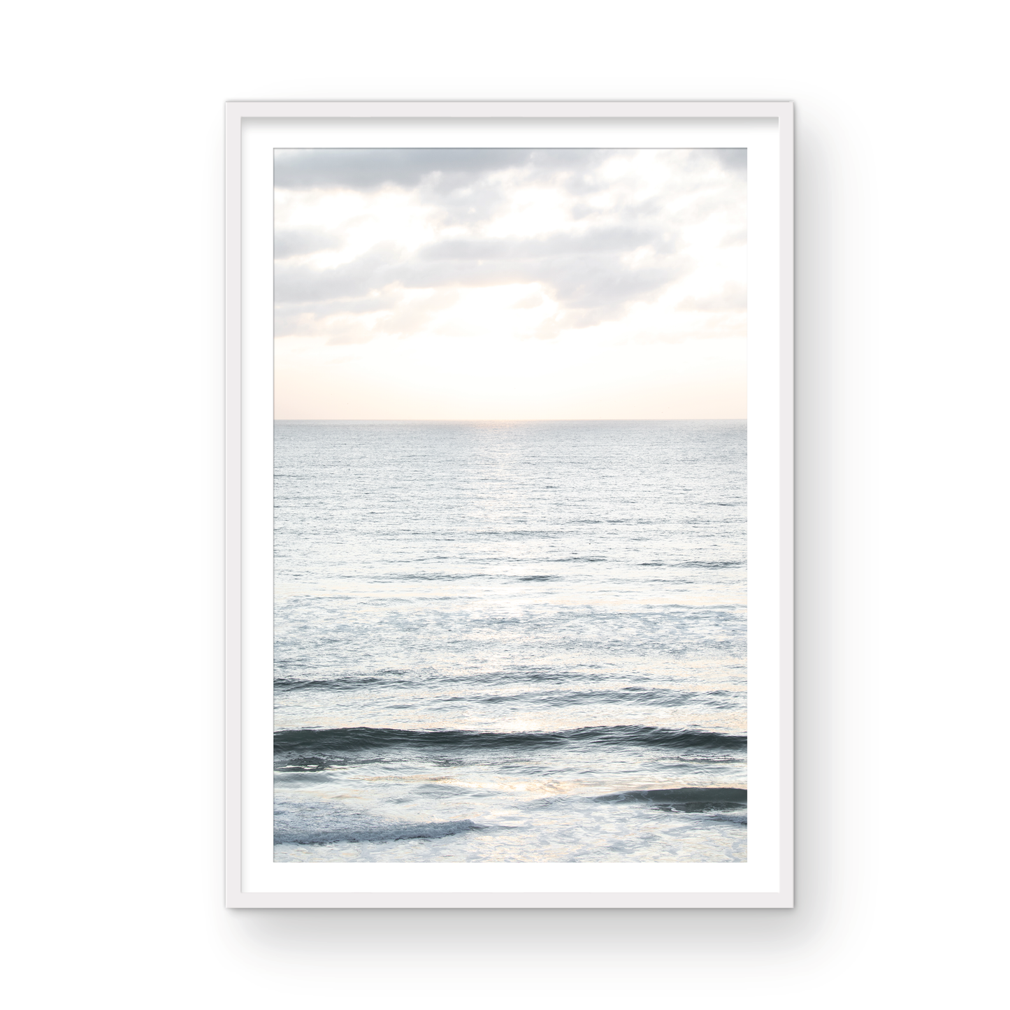 Fine art of vertical landscape print by Southern California photographer Kim Dybczak of Salt Creek Prints, featuring a bright image capturing pale blue ocean waves, light gray clouds in a bright sky. Gentle, small waves in the near and far distance. The sky is a uniform, pale white, creating a soft, overcast atmosphere. Photograph in framed minimalist mock up