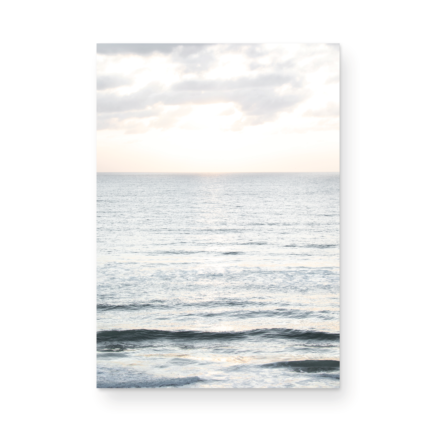 Fine art of vertical landscape print by Southern California photographer Kim Dybczak of Salt Creek Prints, featuring a bright image capturing pale blue ocean waves, light gray clouds in a bright sky. Gentle, small waves in the near and far distance. The sky is a uniform, pale white, creating a soft, overcast atmosphere. Photograph in unframed minimalist mock up
