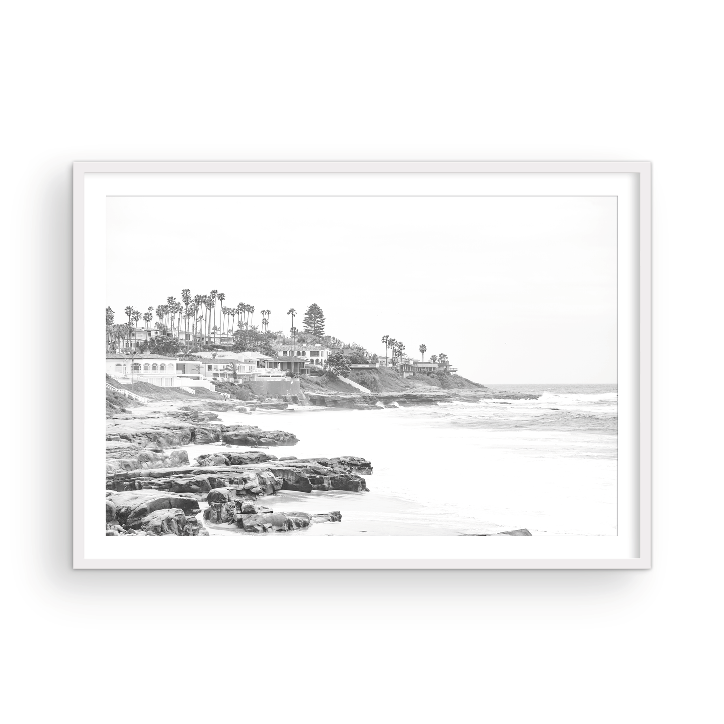 Fine art of WindanSea Beach, La Jolla California horizontal landscape black and white print by Southern California photographer Kim Dybczak of Salt Creek Prints, featuring a powerful waves crashing against the rocky shore of California coast. Beach homes and palm trees sit atop the cliffside, with stairs leading down to a sheltered area. Photograph in minimalist mock up