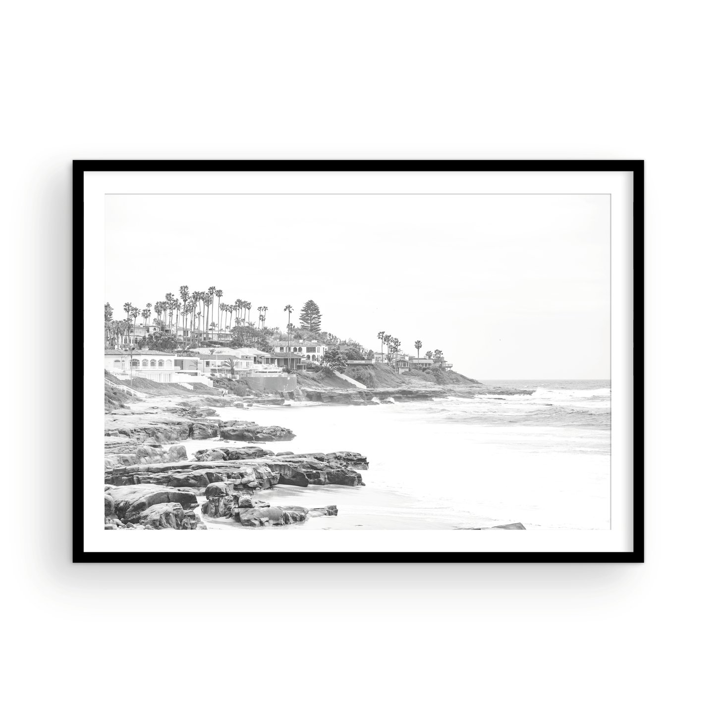 Fine art of WindanSea Beach, La Jolla California horizontal landscape black and white print by Southern California photographer Kim Dybczak of Salt Creek Prints, featuring a powerful waves crashing against the rocky shore of California coast. Beach homes and palm trees sit atop the cliffside, with stairs leading down to a sheltered area. Photograph in minimalist framed mock up