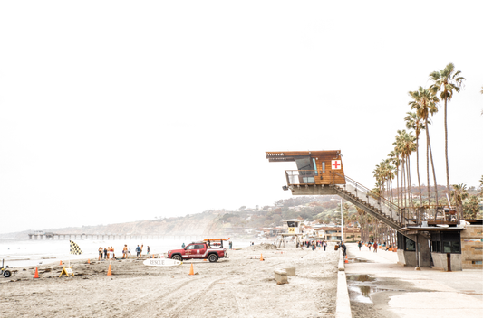 Landscape coastal photography of a minimalist beach with gentle ocean waves on the sand, meeting a hazy, rocky headland or cliff on the right, under a soft, muted sky. This serene seascape provides a calm beach print.