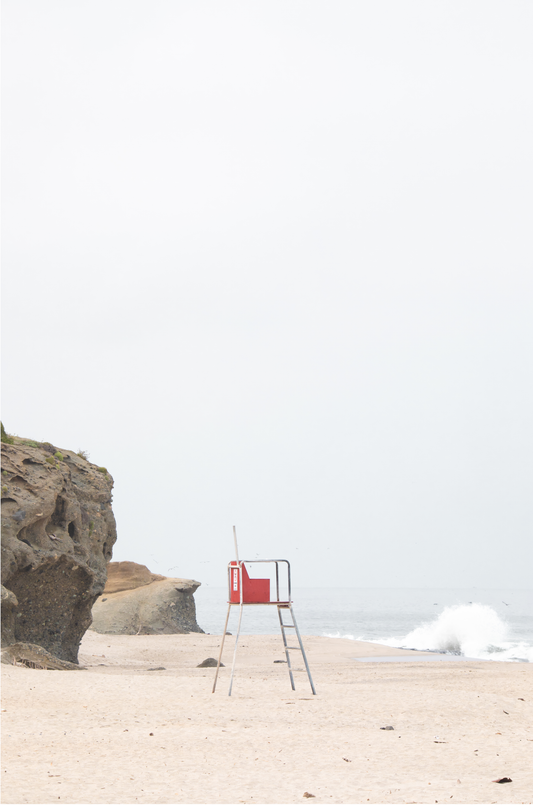 Vertical coastal photography featuring a red and white lifeguard chair and a calm ocean background, located in Laguna California.