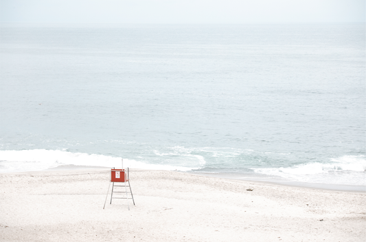 Horizontal coastal photography featuring a red and white lifeguard chair and a calm ocean background, located in Laguna California.